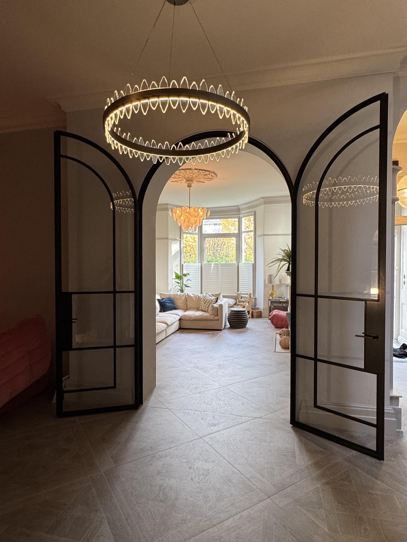 Pair of arched black steel doors standing open beneath a ring chandelier