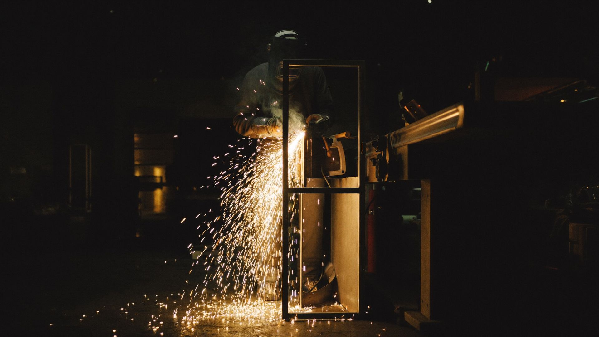 Welder grinding a bespoke steel door frame by hand, sparks cascading across the workshop floor
