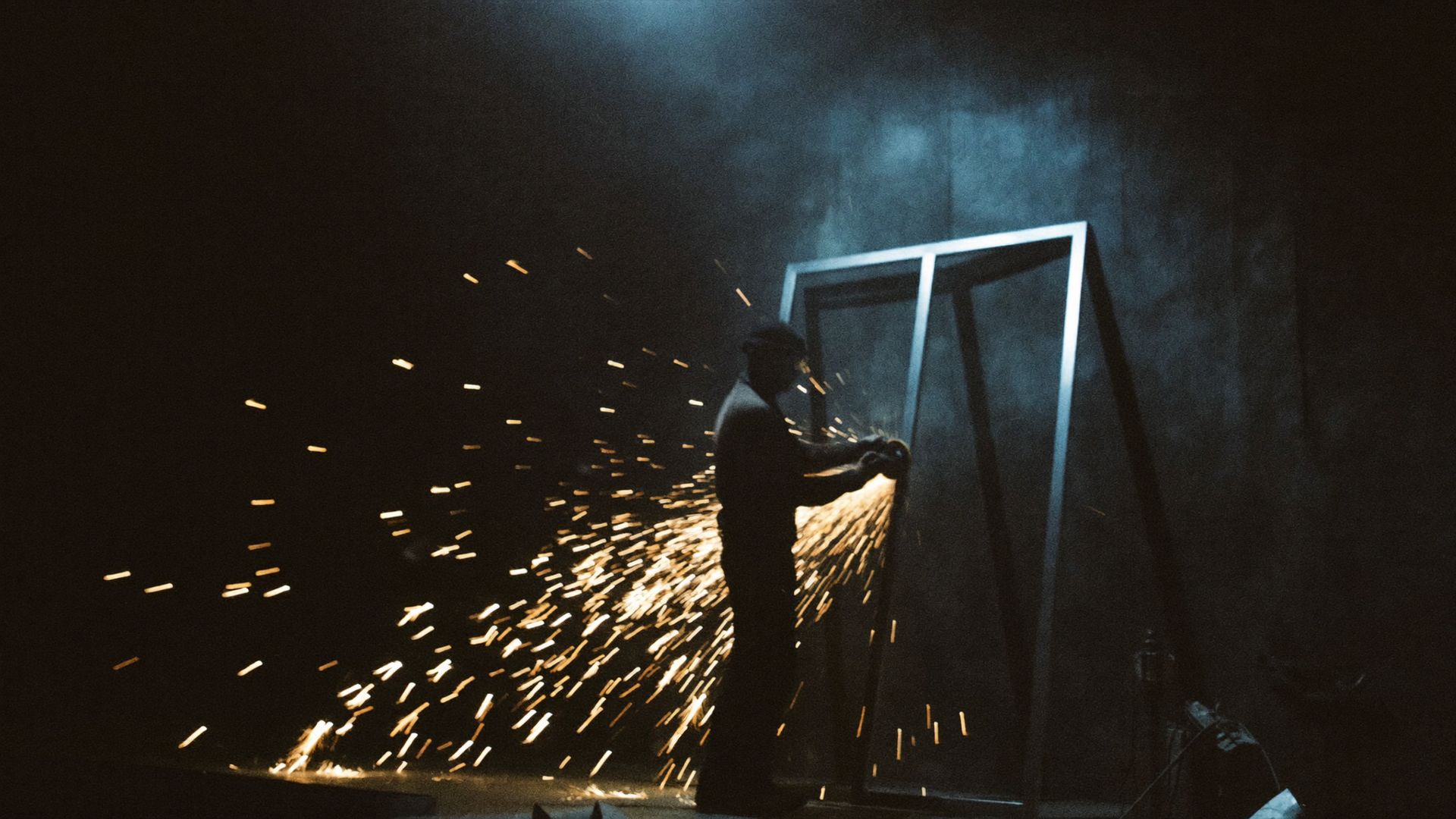 Craftsman fabricating a bespoke steel door frame amid a shower of golden sparks in a dark workshop
