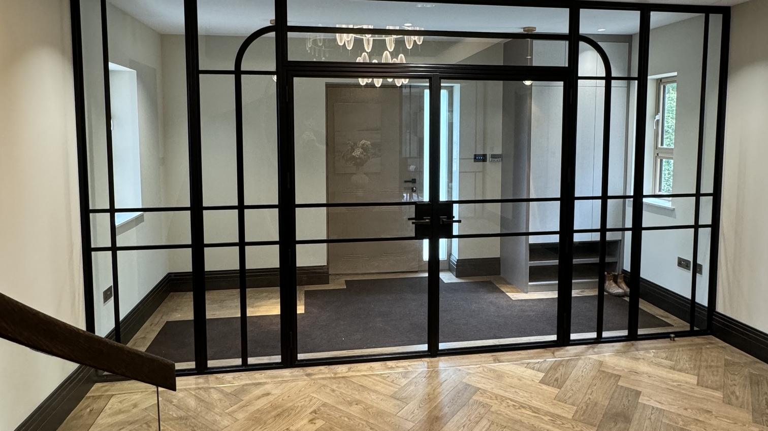 Full-width internal steel glazed screen beneath a chandelier, herringbone oak floor