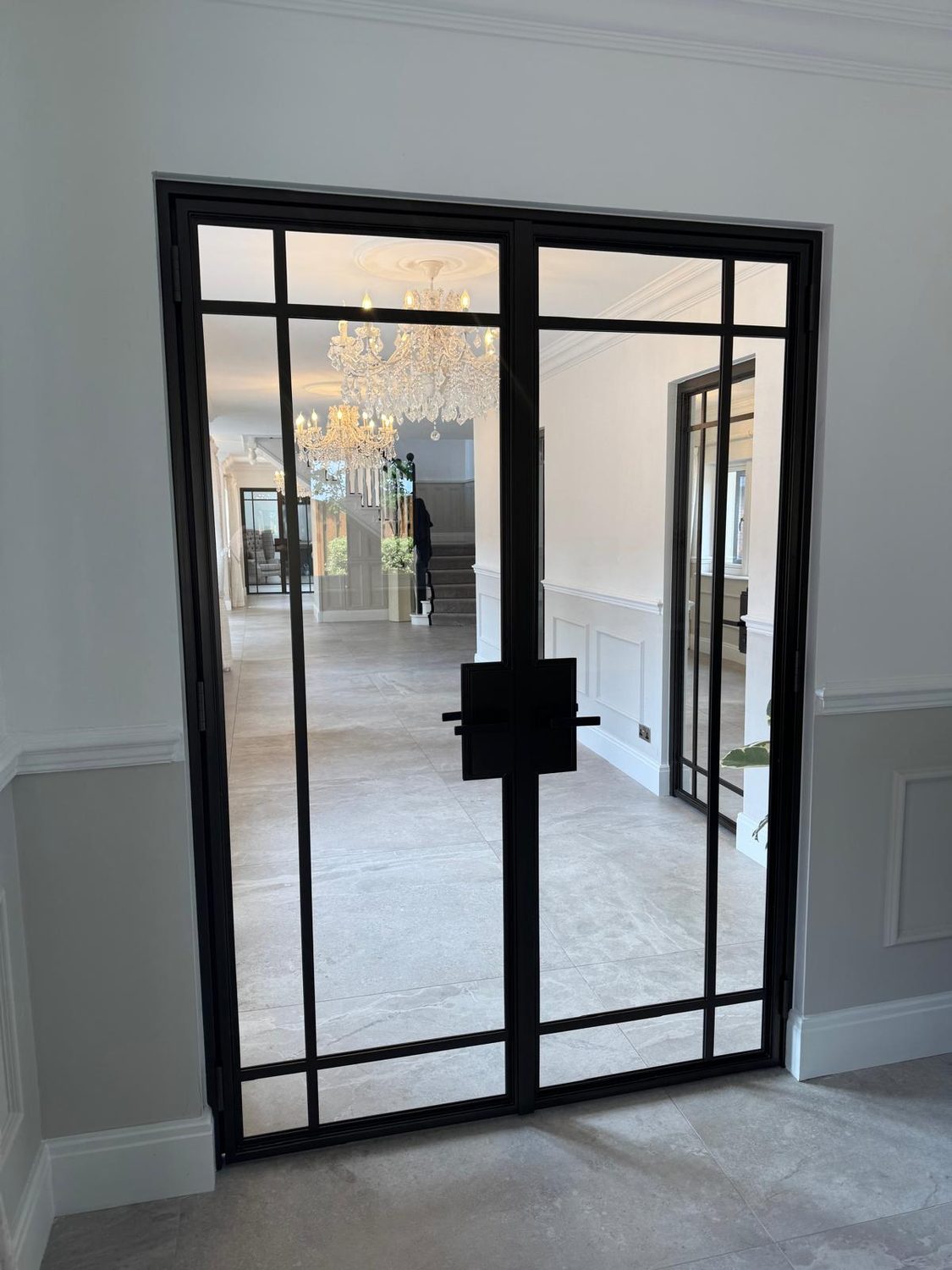 Internal steel double doors opening onto a hallway beneath a chandelier