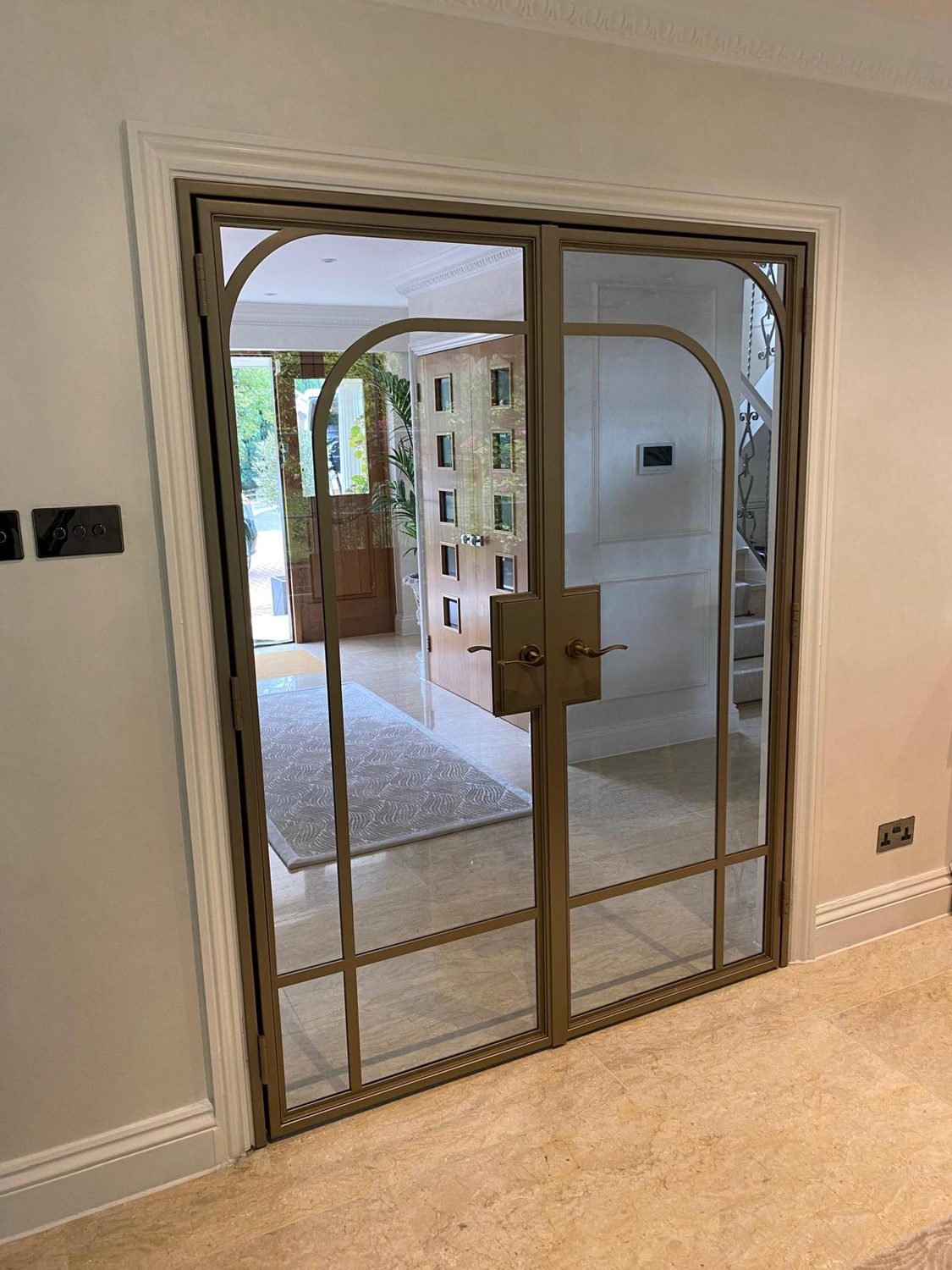 Internal steel doors with arched glazing bars in a bronze finish, opening onto an entrance hall
